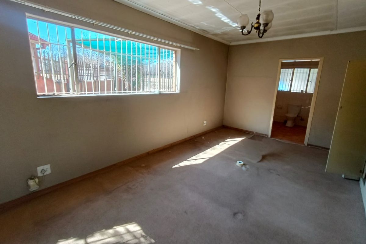 An empty bedroom featuring carpet flooring, security bars on the window, and an attached bathroom entrance.