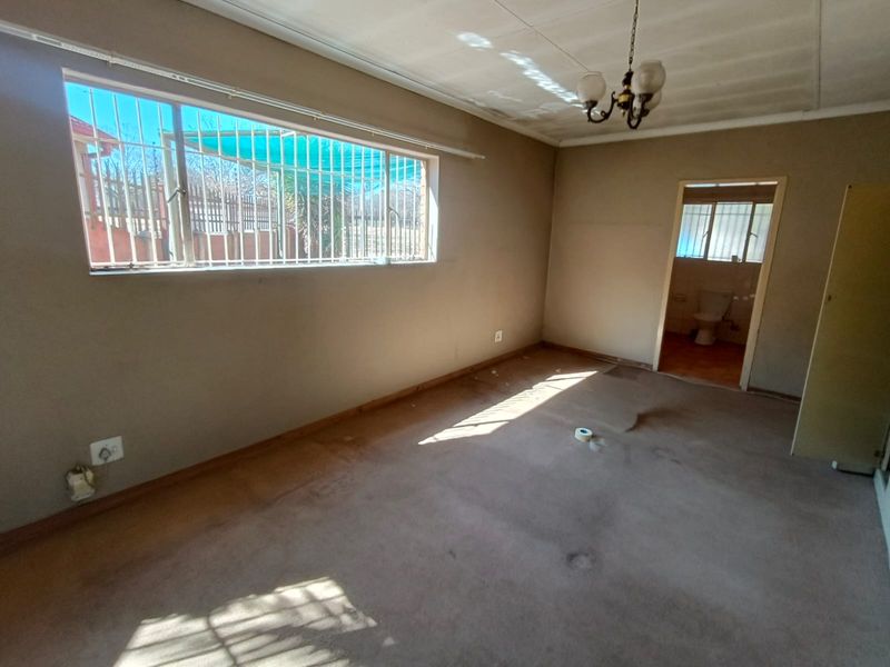 An empty bedroom featuring carpet flooring, security bars on the window, and an attached bathroom entrance.
