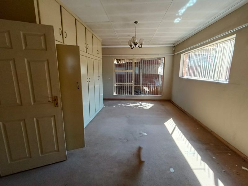 Spacious bedroom featuring extensive built-in cabinetry, security bars on windows, and neutral carpeting, offering a blank canvas for renovation.