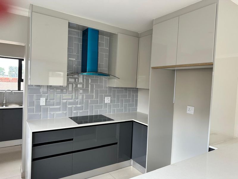 Modern kitchen featuring high-gloss cabinetry, quartz countertops, a herringbone subway tile backsplash, and a contemporary blue extractor fan.