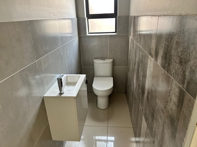 A compact, modern guest bathroom featuring contemporary grey wall tiles, a wall-mounted vanity with basin, and a clean white toilet.