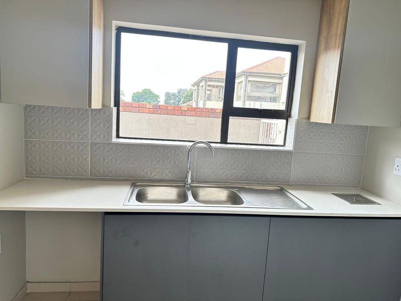 Modern kitchen area featuring a double bowl stainless steel sink, stone countertops, textured tile backsplash, and contemporary cabinetry.