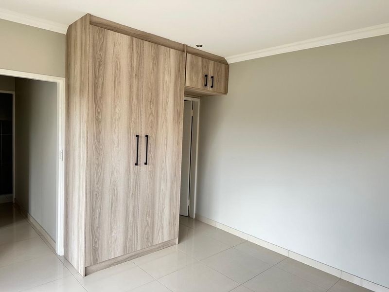 A bright, modern bedroom featuring neutral tiled flooring and contemporary wood-finish built-in cupboards with sleek black hardware.