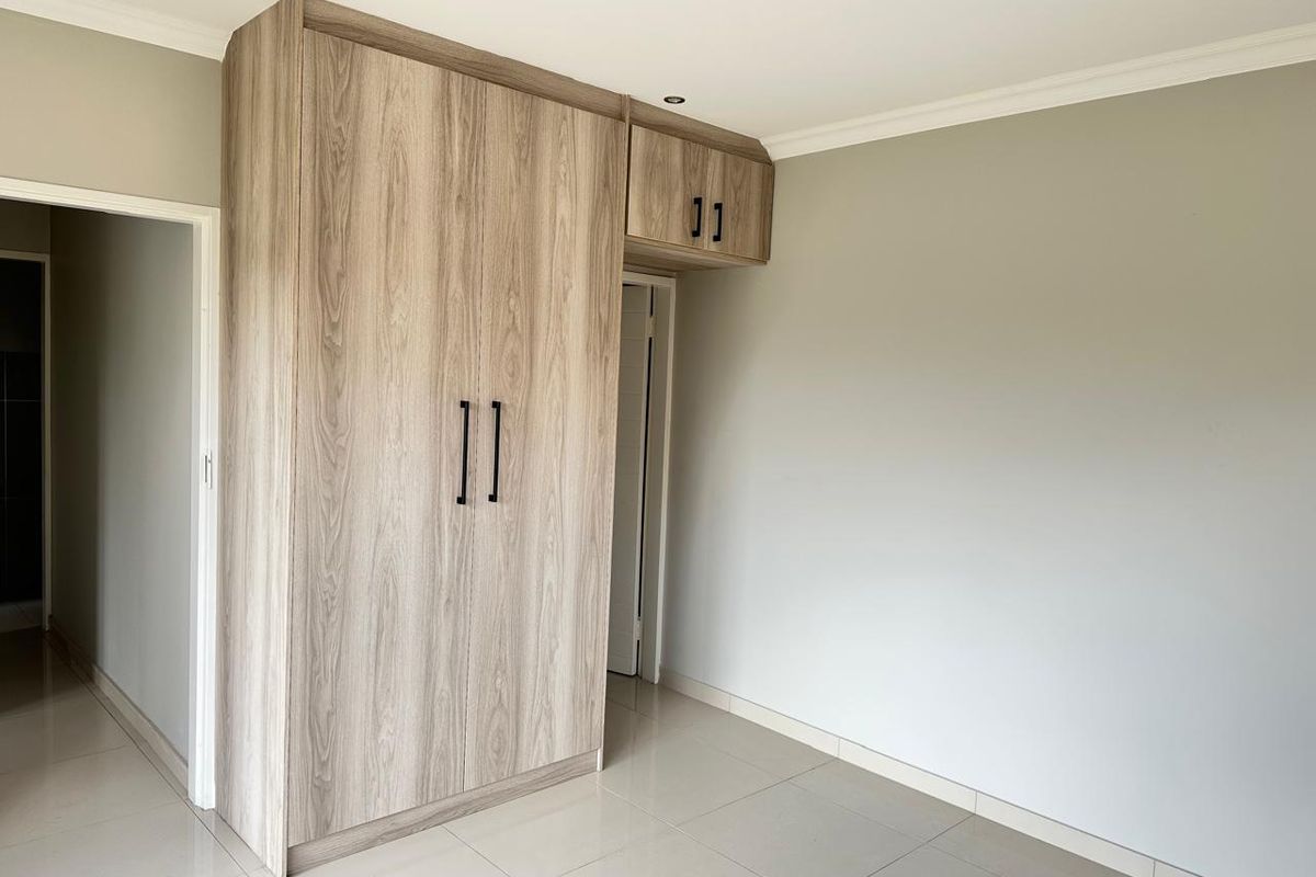 A bright, modern bedroom featuring neutral tiled flooring and contemporary wood-finish built-in cupboards with sleek black hardware.