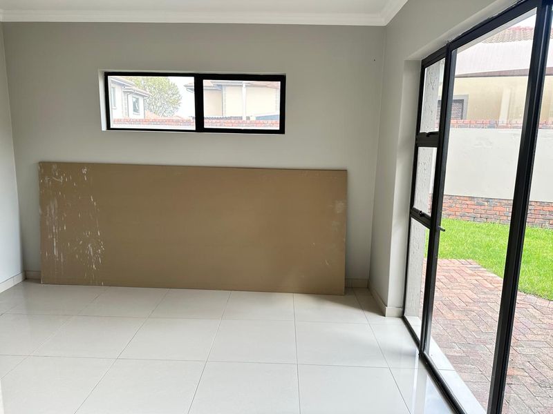 An empty living room featuring neutral tiled flooring, modern black aluminium window frames, and a sliding door providing access to the rear garden.