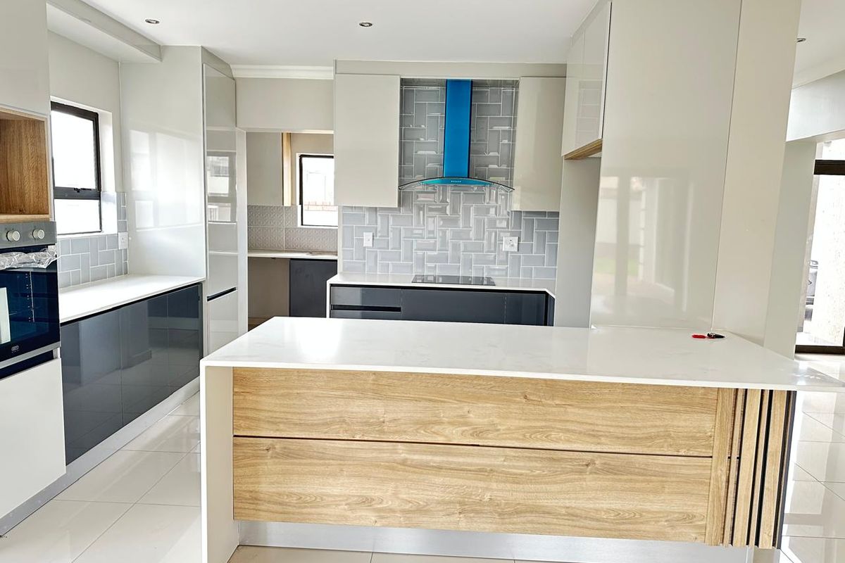 Modern kitchen featuring a central island, built-in oven, extractor fan, sleek cabinetry, and high-quality quartz countertops with a stylish tiled backsplash.
