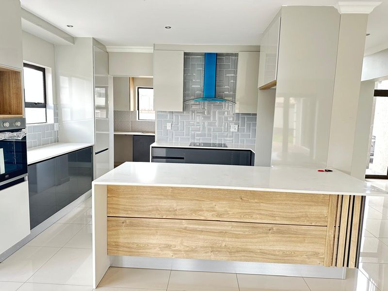 Modern kitchen featuring a central island, built-in oven, extractor fan, sleek cabinetry, and high-quality quartz countertops with a stylish tiled backsplash.