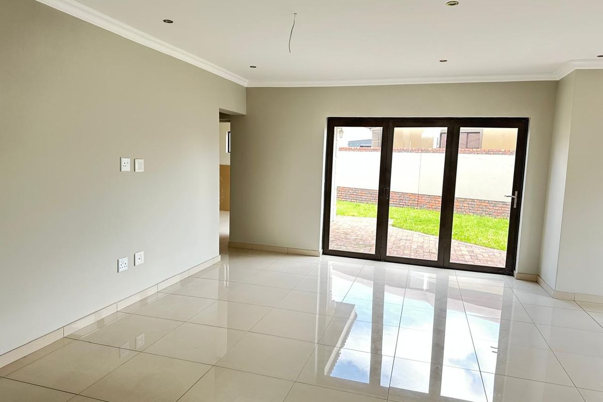 A bright, empty living room featuring polished porcelain floor tiles, recessed downlights, and large aluminium stacker doors providing access to the rear garden.