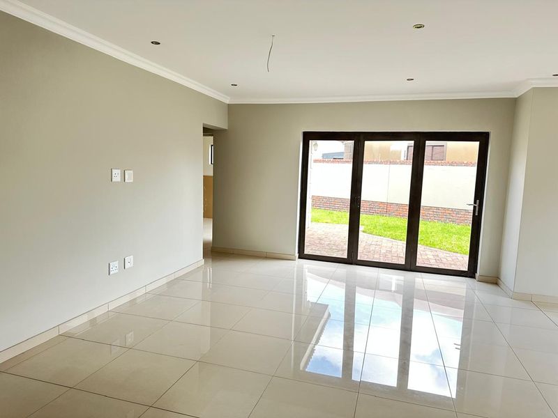 A bright, empty living room featuring polished porcelain floor tiles, recessed downlights, and large aluminium stacker doors providing access to the rear garden.