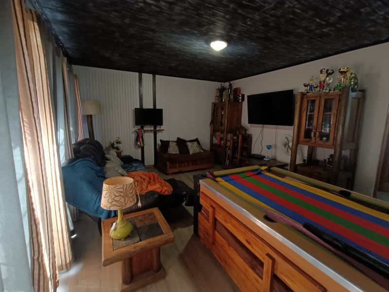 A living room featuring dark timber ceiling panels, vertical wall paneling, and laminate flooring, offering a rustic aesthetic with potential for modernization.