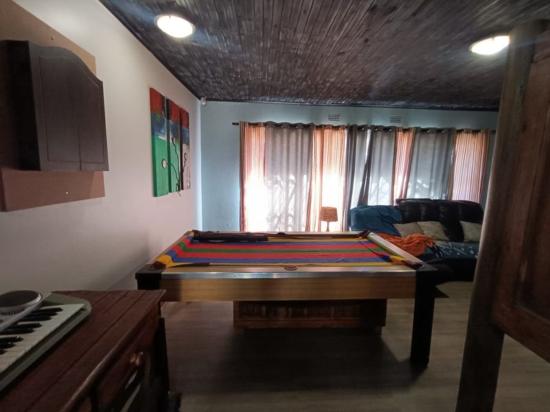Spacious living area featuring a dark timber-clad ceiling, laminate flooring, and large windows allowing for natural light.