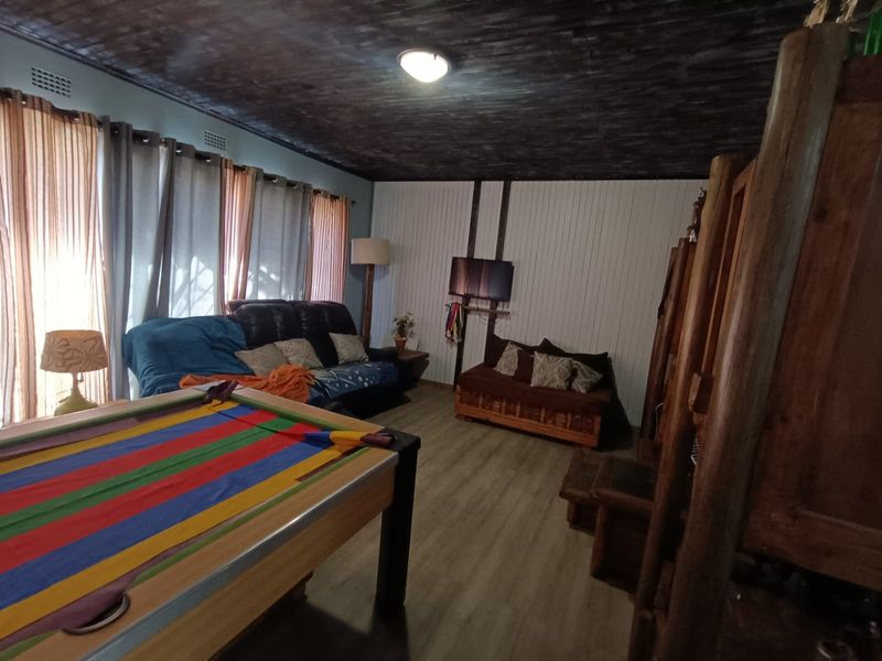 A living area featuring timber-look flooring, a dark painted timber ceiling, and vertical wall paneling, offering a rustic aesthetic with potential for modernization.