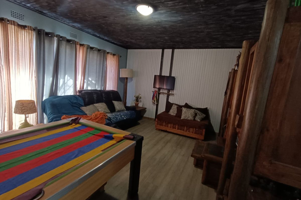 A living area featuring timber-look flooring, a dark painted timber ceiling, and vertical wall paneling, offering a rustic aesthetic with potential for modernization.