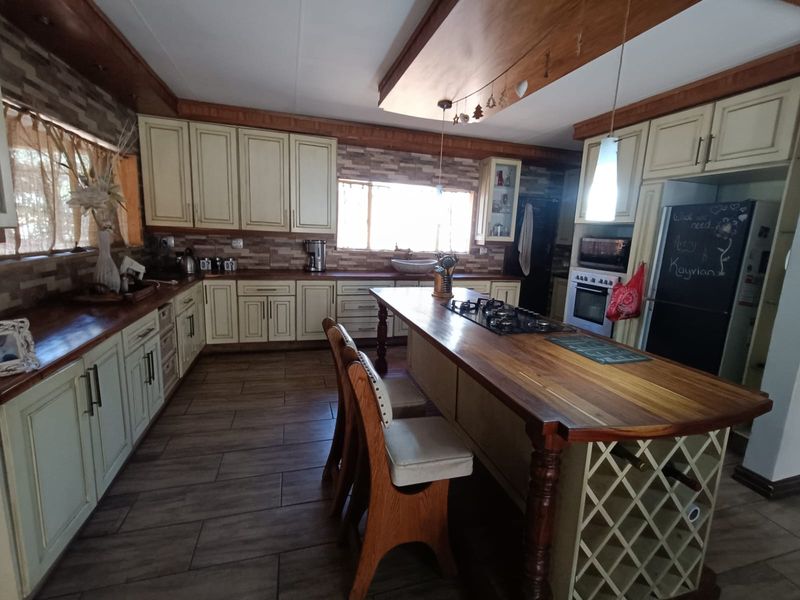 Spacious kitchen featuring wooden countertops, a central island with a built-in gas hob, integrated appliances, and tiled flooring with a warm, rustic aesthetic.
