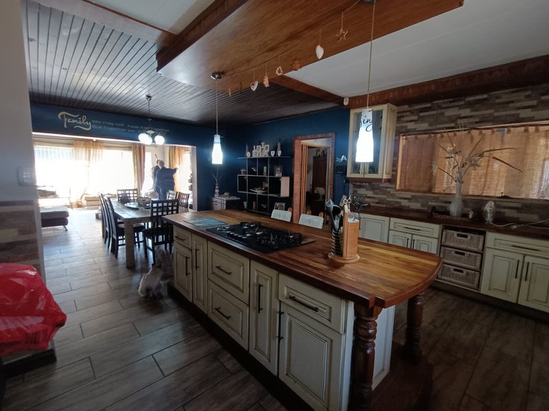 Spacious open-plan kitchen and dining area featuring a large timber-topped island with integrated gas hob, stone veneer accents, and warm timber ceiling detailing.