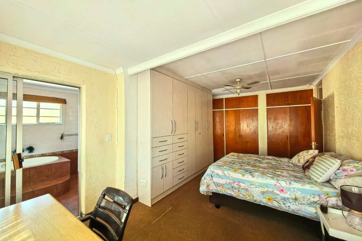 Spacious bedroom featuring extensive built-in cabinetry, a ceiling fan, and an adjoining en-suite bathroom with a built-in bathtub.