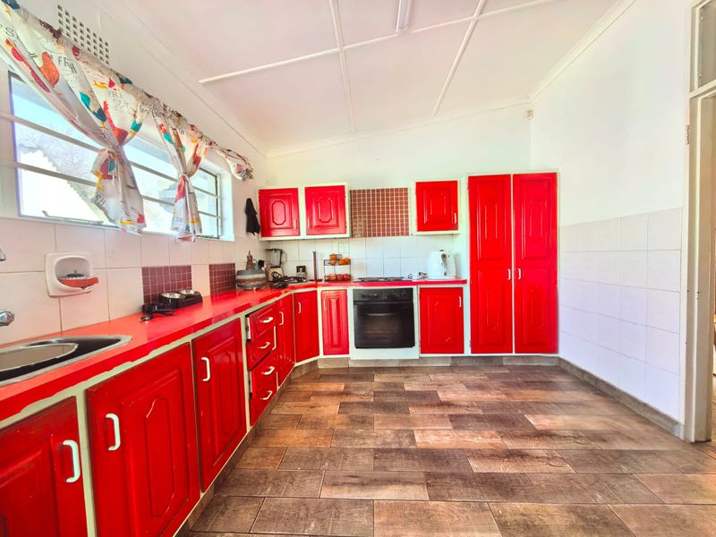 A dated kitchen featuring bright red cabinetry, integrated oven, hob, tiled splashbacks, and wood-look tiled flooring.