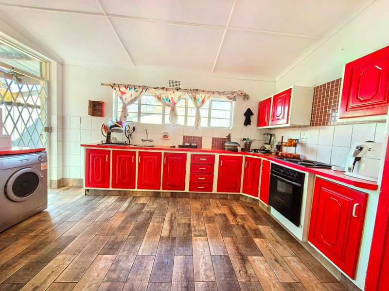 A functional kitchen featuring bright red cabinetry, tiled splashbacks, built-in oven and hob, and wood-look tiled flooring with direct access to the exterior.