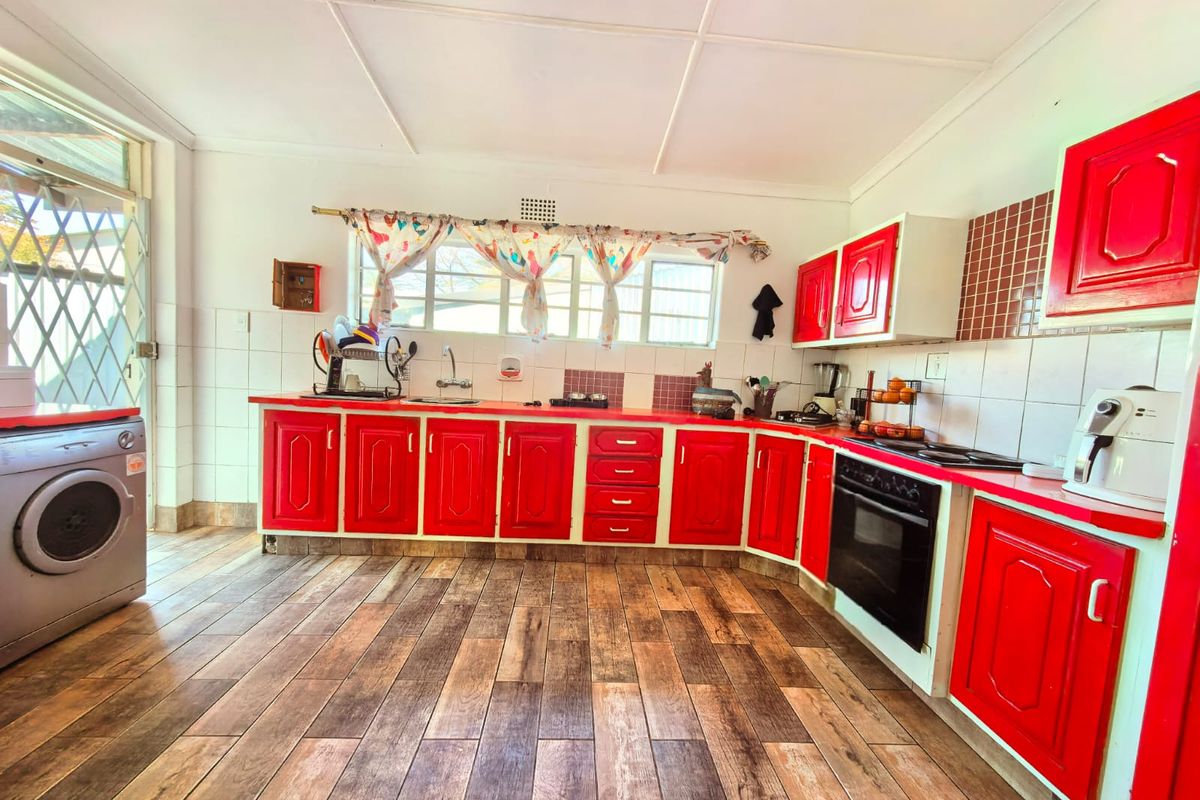 A functional kitchen featuring bright red cabinetry, tiled splashbacks, built-in oven and hob, and wood-look tiled flooring with direct access to the exterior.