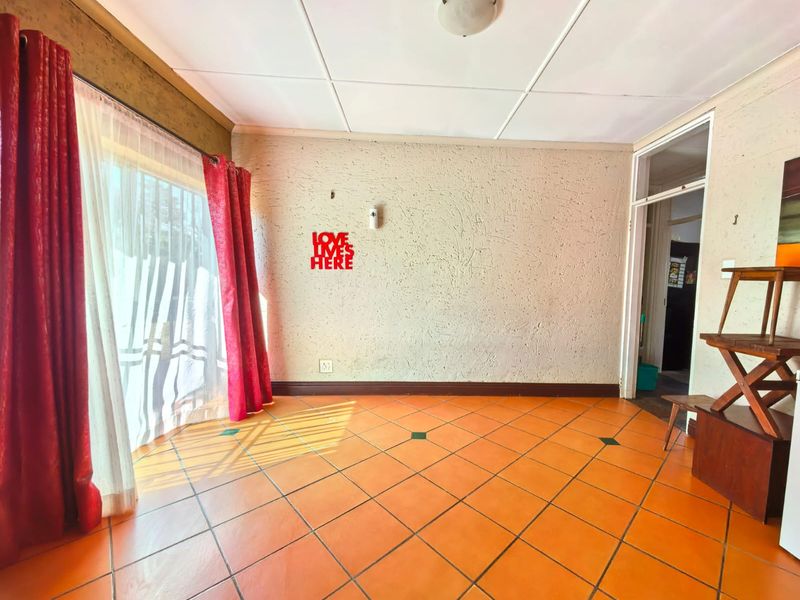 An empty living room featuring orange tiled flooring, textured walls, and a sliding glass door providing natural light.