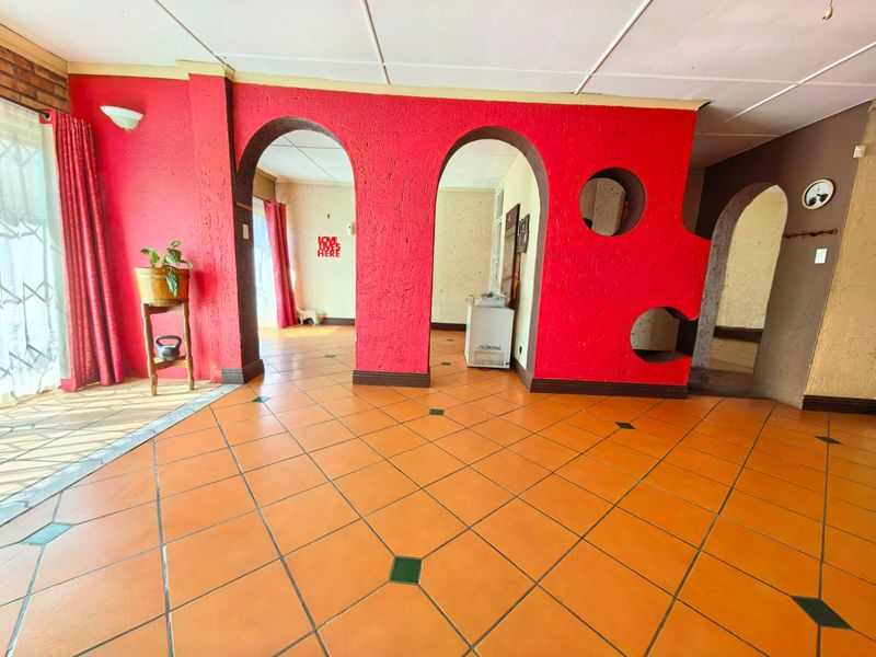 Spacious living area featuring distinctive arched doorways, textured red walls, and terracotta tile flooring, offering a unique layout with potential for modern updates.
