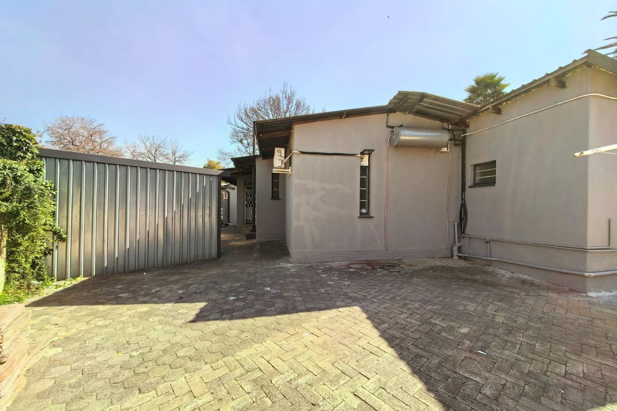 Rear exterior view of the property featuring a paved courtyard, corrugated metal fencing, and external utility installations including a geyser and air conditioning unit.