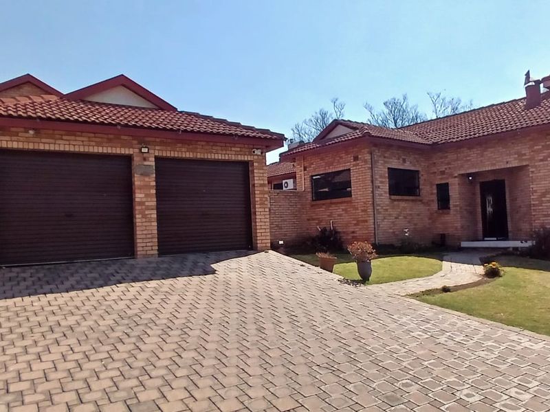 Front view of a face brick house featuring a double garage, paved driveway, and a neat front garden with a paved walkway.
