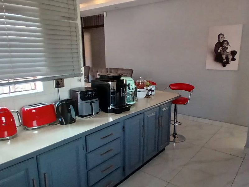 A functional kitchen area featuring blue built-in cabinetry, stone countertops, and tiled flooring, illuminated by natural light through venetian blinds.