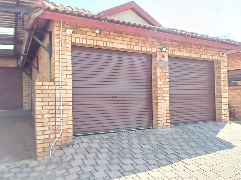 A well-maintained brick exterior featuring a double garage with roller doors and an adjacent covered carport area with a paved driveway.