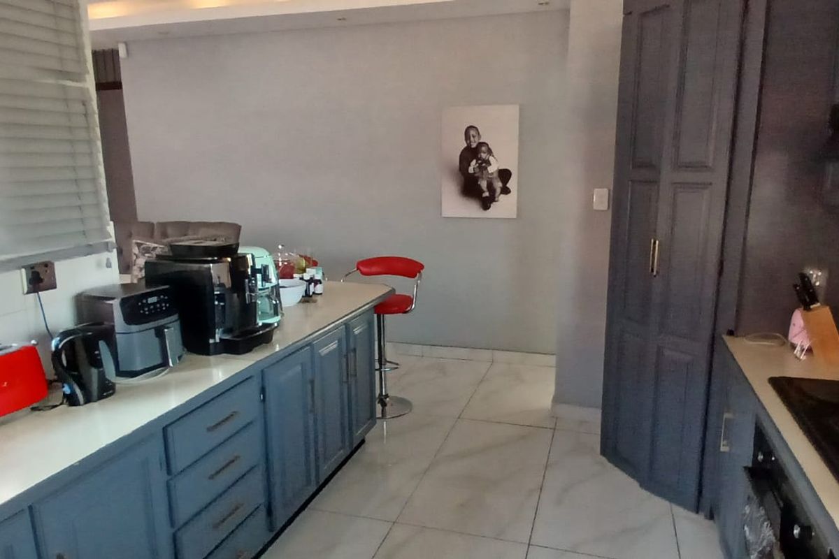 A modern kitchen featuring dark grey cabinetry, stone countertops, an integrated hob with extractor fan, and light-colored tiled flooring.