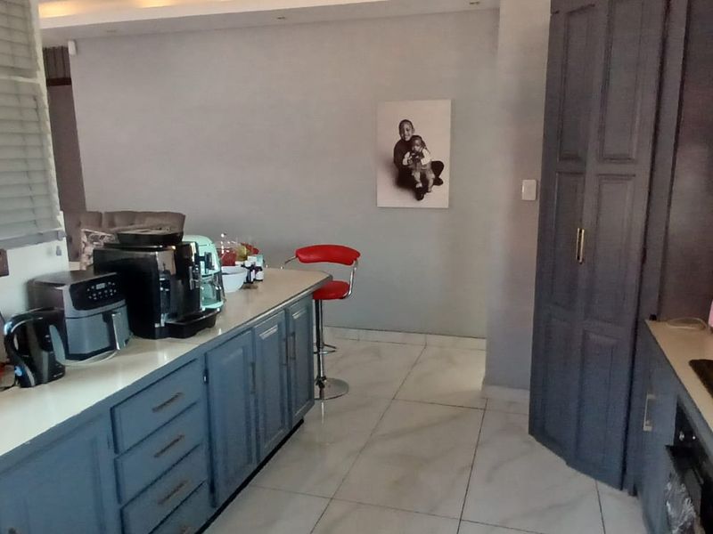 A modern kitchen featuring dark grey cabinetry, stone countertops, an integrated hob with extractor fan, and light-colored tiled flooring.