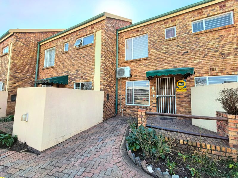 Front exterior view of a face brick townhouse featuring a paved walkway, security gate, and installed air conditioning unit.