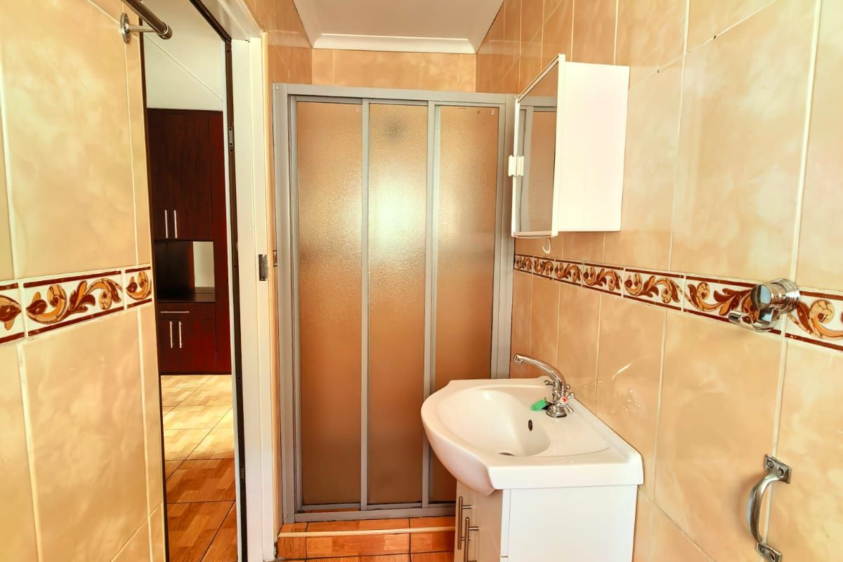 A functional bathroom featuring a shower enclosure, vanity basin, and full-height wall tiling with decorative border accents.