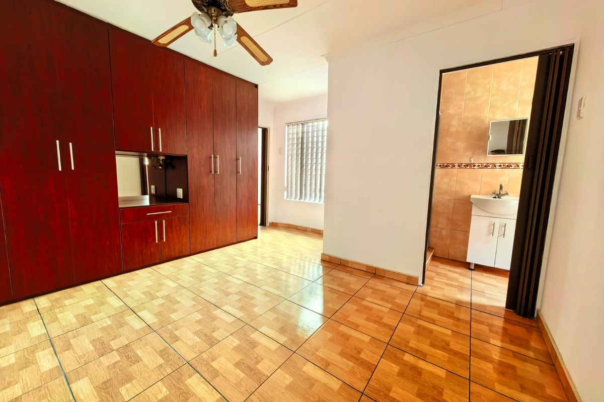 Spacious bedroom featuring extensive built-in wooden cabinetry, tiled flooring, a ceiling fan, and direct access to an en-suite bathroom.