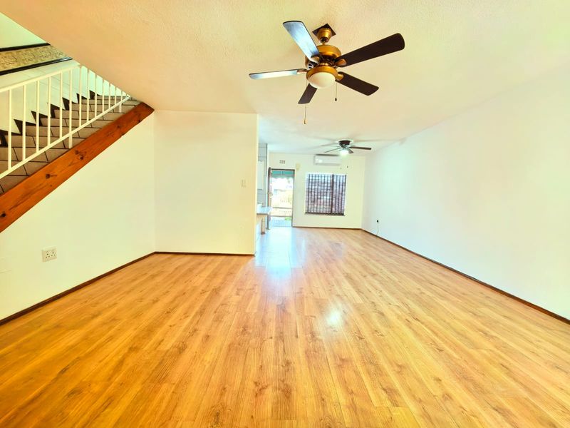 Spacious open-plan living area featuring laminate flooring, ceiling fans, a split-system air conditioner, and a staircase with a metal railing.