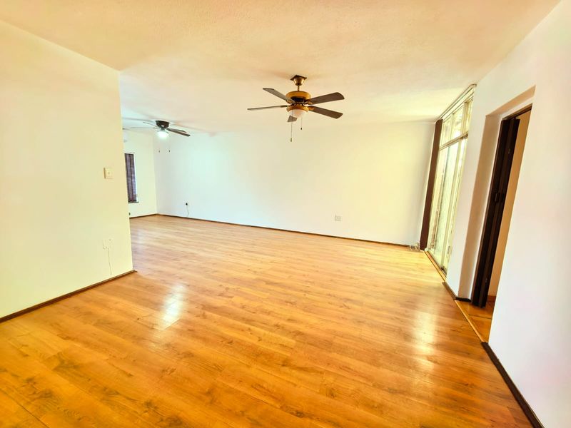 Spacious, empty living area featuring warm-toned laminate flooring, dual ceiling fans, and large sliding glass doors providing natural light.