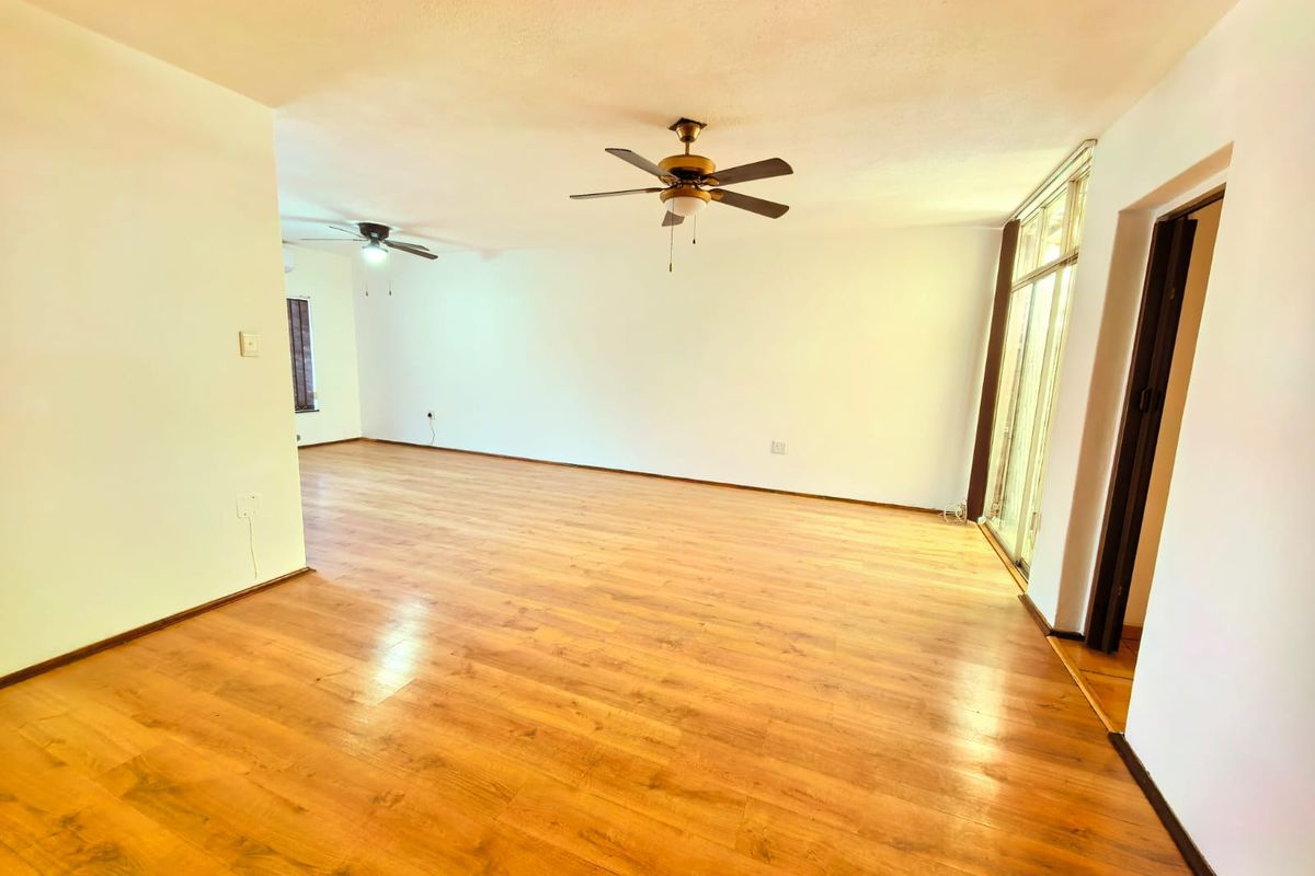 Spacious, empty living area featuring warm-toned laminate flooring, dual ceiling fans, and large sliding glass doors providing natural light.
