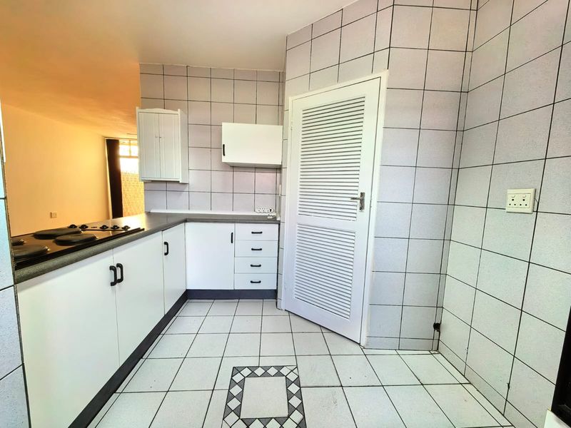 A dated kitchen featuring white cabinetry, tiled walls and flooring, and a built-in hob, offering a blank canvas for modern renovation.