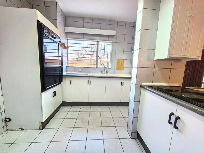 A functional kitchen featuring built-in cabinetry, a double sink, an integrated oven, and an electric hob with tiled finishes throughout.