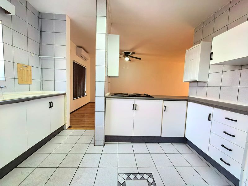 A functional kitchen featuring white built-in cabinetry, tiled flooring, and a built-in hob, with an open-plan layout leading to an adjacent living area.