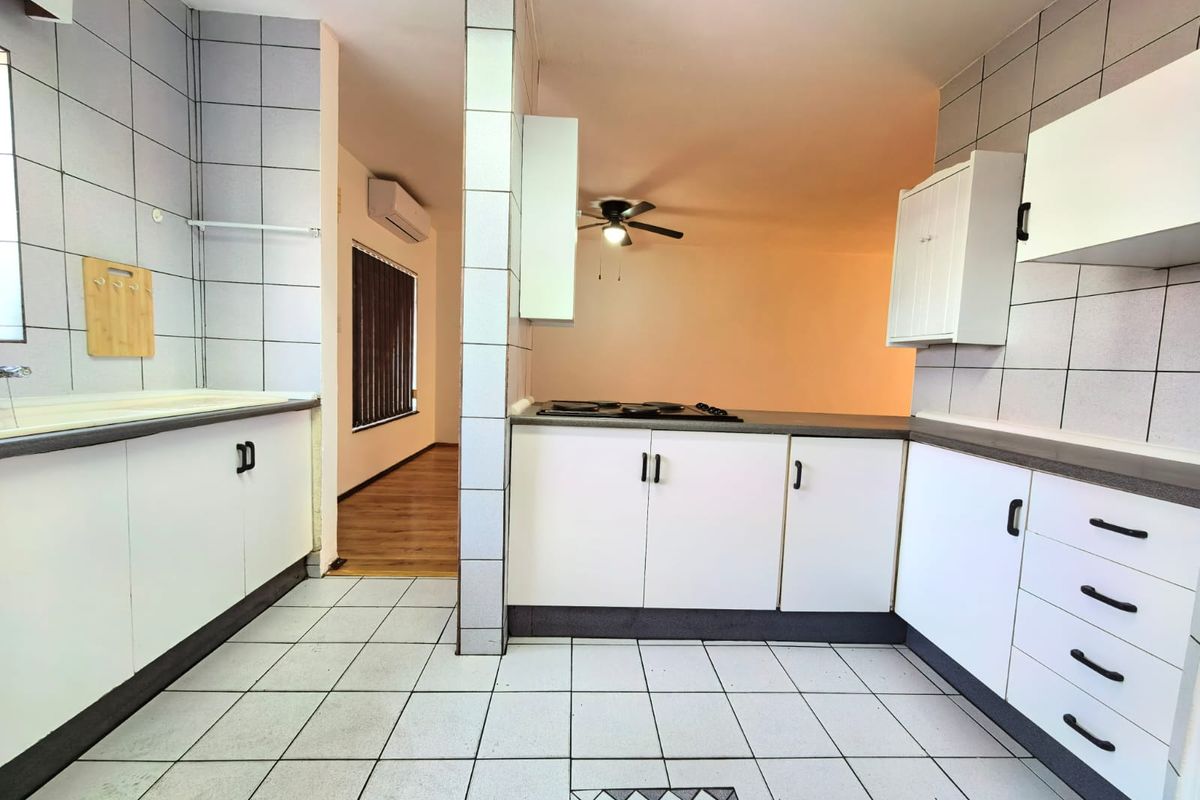A functional kitchen featuring white built-in cabinetry, tiled flooring, and a built-in hob, with an open-plan layout leading to an adjacent living area.