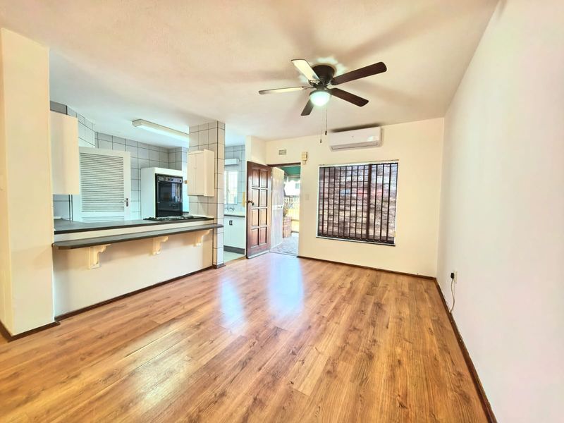 Open-plan living area featuring laminate flooring, a ceiling fan, air conditioning, and a breakfast bar connecting to the kitchen space.