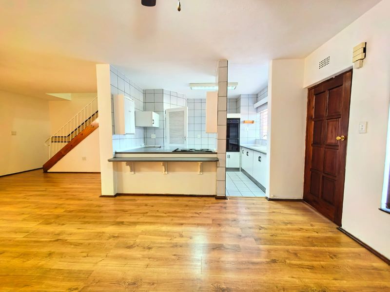 Open-plan living area featuring laminate flooring, a staircase, and a functional kitchen with built-in cabinetry, oven, and hob.