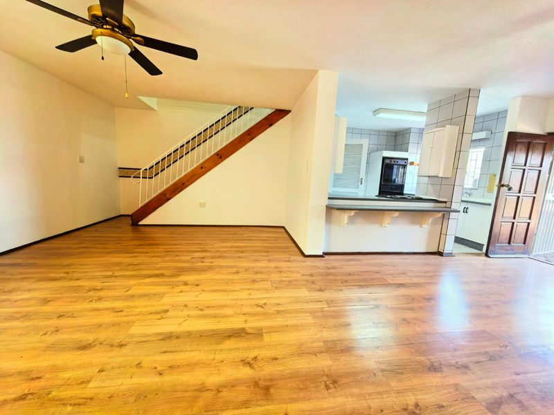 Open plan living area featuring laminate flooring, a ceiling fan, a staircase, and a breakfast bar connecting to the kitchen.