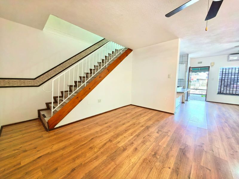 Open plan living area featuring laminate flooring, a staircase with metal balustrade, and direct access to the rear exterior.