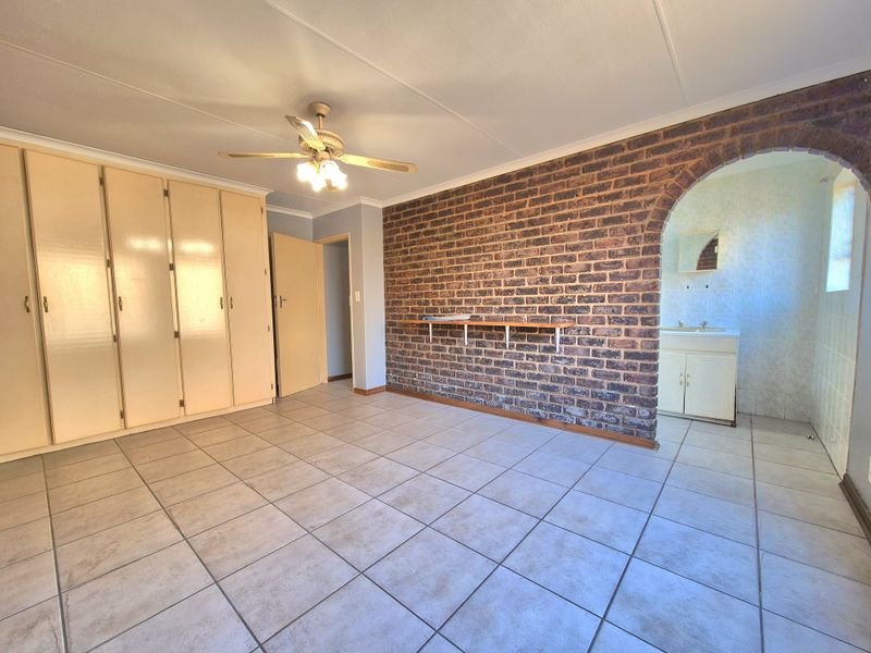 Spacious bedroom featuring an exposed brick wall, built-in cupboards, tiled flooring, and an open archway leading to an en-suite vanity area.