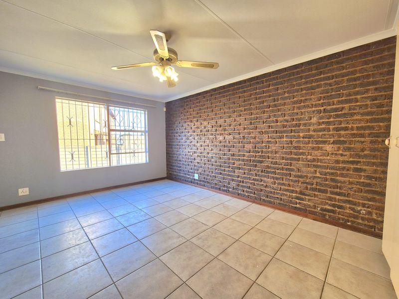 Spacious bedroom featuring a distinctive exposed brick wall, neutral tiled flooring, and a ceiling fan, offering a clean and versatile living space.