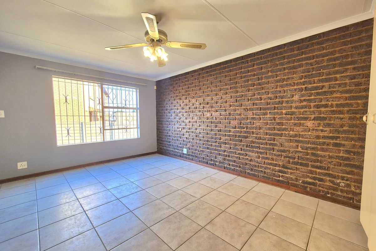 Spacious bedroom featuring a distinctive exposed brick wall, neutral tiled flooring, and a ceiling fan, offering a clean and versatile living space.