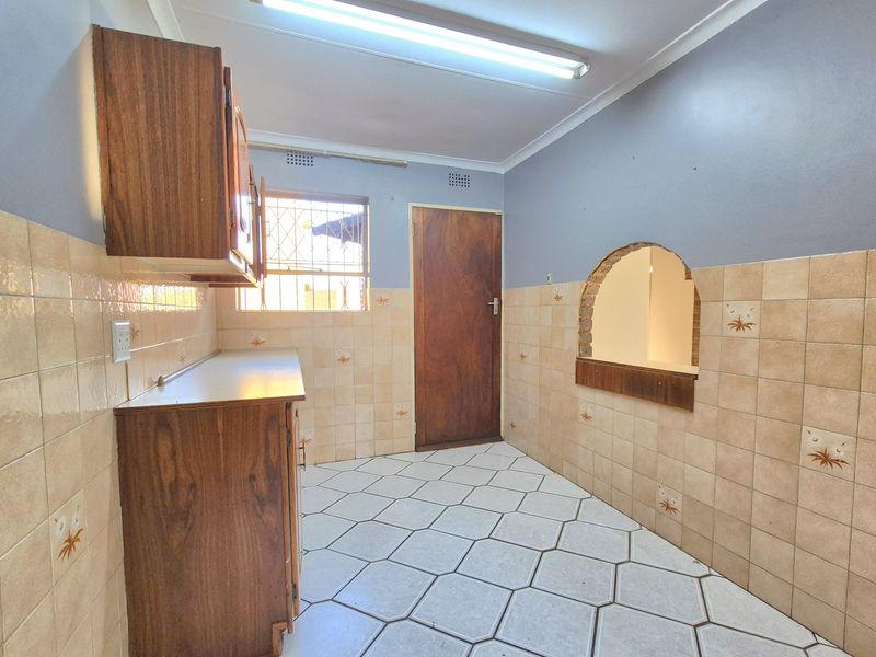 A vacant kitchen featuring dated wooden cabinetry, tiled walls, and a unique archway serving hatch, offering a blank canvas for modern renovation.