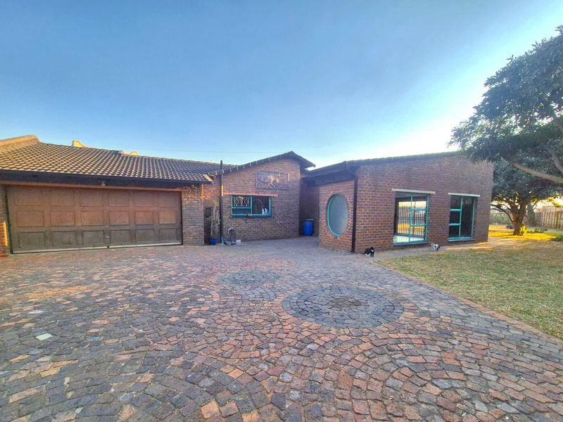 Front exterior view of a brick house featuring a large cobblestone driveway, double garage, and distinctive circular window design.